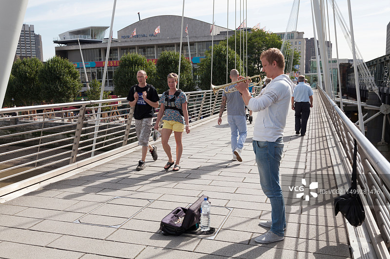 街头艺人在泰晤士河上的金禧人行桥上吹小号图片素材