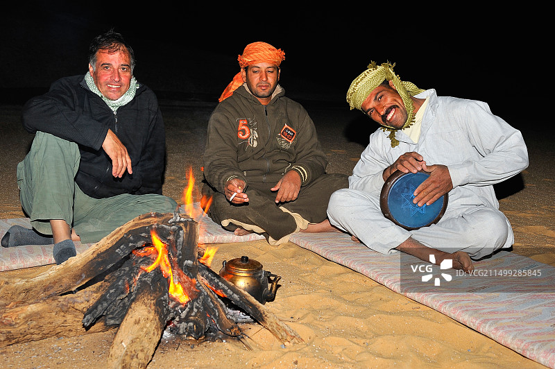 在埃及白色沙漠过夜期间,人们围坐在篝火旁,听着埃及音乐家用坦坦鼓演奏图片素材