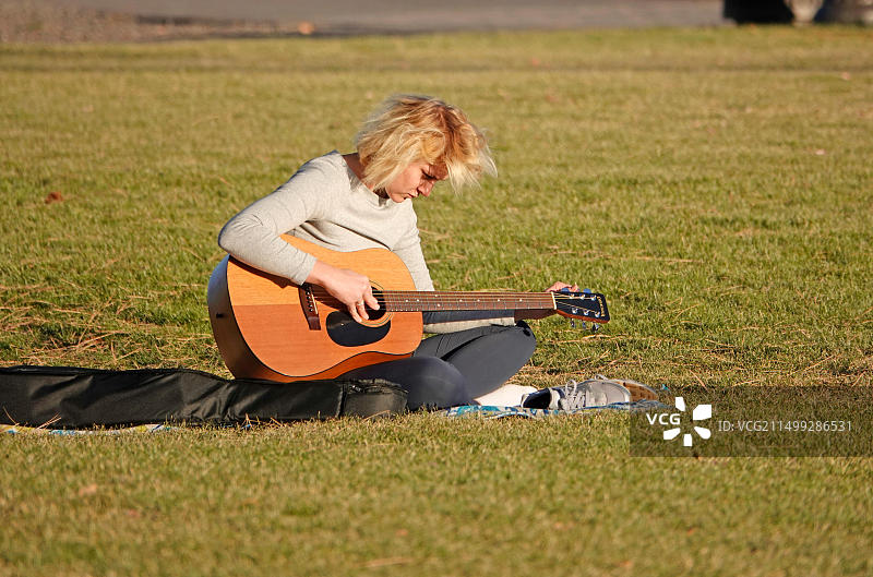 年轻女子在俄勒冈州本德市德舒特斯河畔的公园里调吉他图片素材