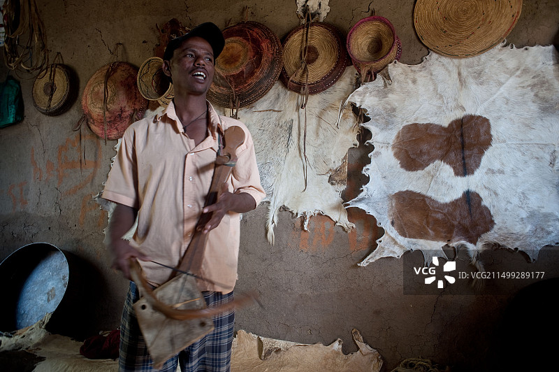 吟游诗人演奏当地乐器并歌唱，身后墙上挂着牛皮（埃塞俄比亚）图片素材