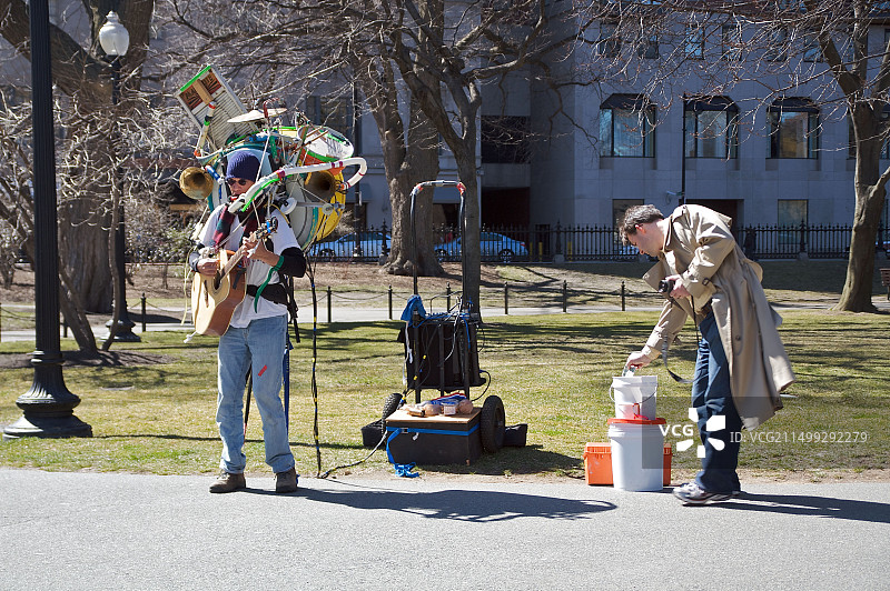 在波士顿公共花园，男人给用吉他和其他乐器表演的音乐家小费图片素材