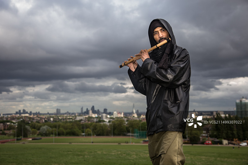 混血男子在汉普斯特德荒原的长草中吹长笛，头戴头巾，身穿黑色亮面夹克图片素材