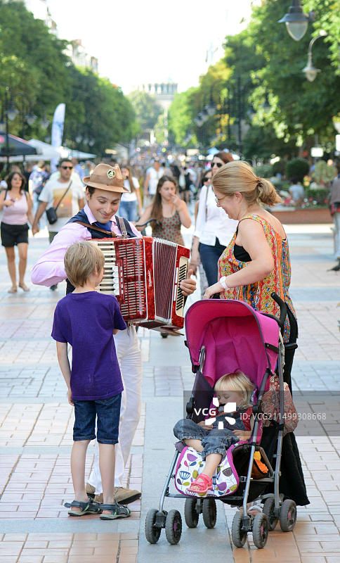 在索非亚维托沙大道上手风琴演奏者与好奇的男孩互动（保加利亚）图片素材