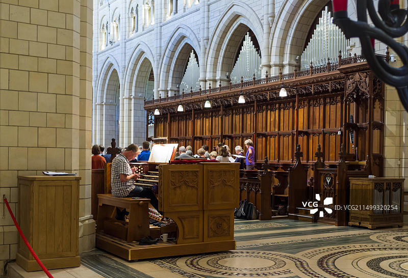 管风琴师坐在修道院的管风琴旁，看着手机，背景是唱诗班。图片素材