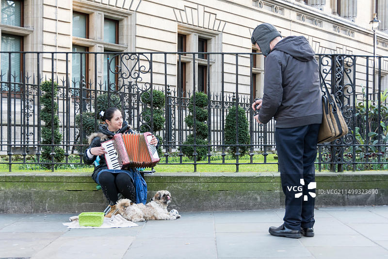 在伦敦国家肖像馆外拉手风琴的女街头艺人和她的宠物拉布拉多犬图片素材