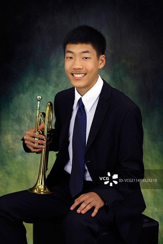 穿着西装，打着领带，拿着小号的亚洲青少年图片素材