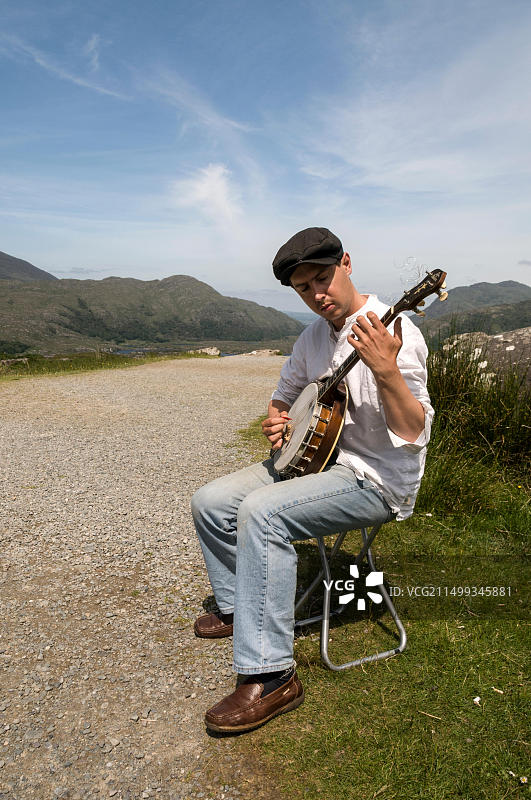 一位年轻的爱尔兰街头艺人在爱尔兰南部肯梅尔以北几英里的女士观景点附近演奏班卓琴。他为了游客的利益演奏班卓琴图片素材