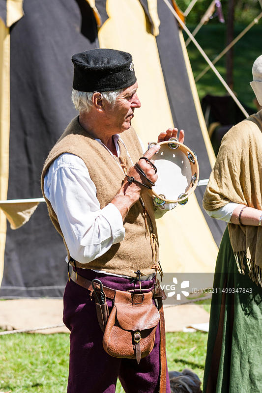 中世纪重演活动：装扮成吟游乐师的中年男子在阳光下演奏铃鼓图片素材