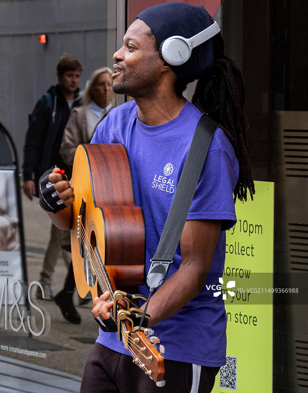 年轻的黑人男子，街头艺人，在牛津马莎百货外弹吉他唱歌图片素材