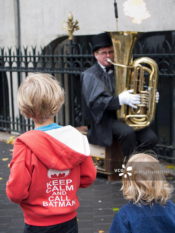 伦敦街头：男子吹奏大号，孩童路过，雨中街头音乐人的真实写照图片素材