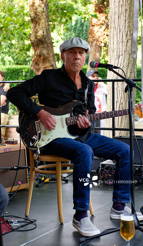 在特威克纳姆美食节上，吉他手和歌手坐在舞台上的麦克风前，戴着扁帽图片素材