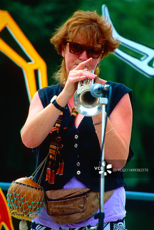 穿着色彩鲜艳服装，吹小号的年轻女人图片素材