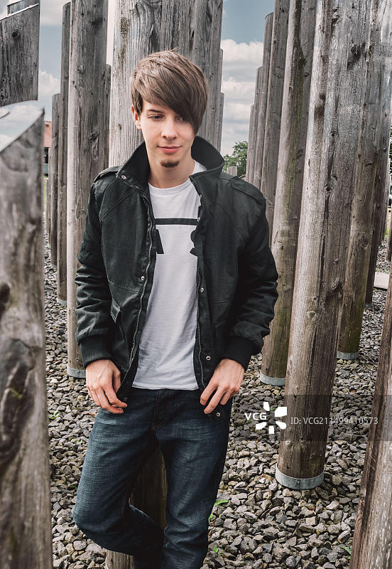 年轻的摇滚音乐家兼歌手靠在木柱上，留着棕色头发和胡须图片素材