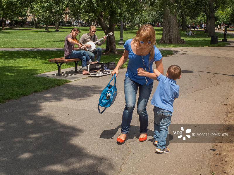 在波士顿公共花园里，母亲和儿子随着两位街头音乐家的声音跳舞图片素材