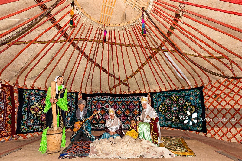 哈萨克斯坦人在阿拉木图的游牧毡房里，一个女人在纺羊毛，一个男人在演奏当地的冬不拉乐器图片素材