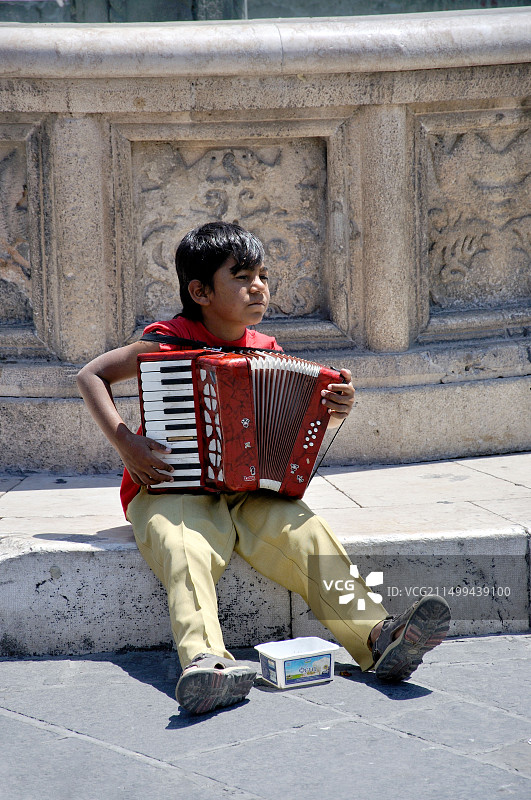 男孩在希腊罗德市伊波克拉图斯广场的老城区卡斯特拉尼亚喷泉旁演奏手风琴图片素材