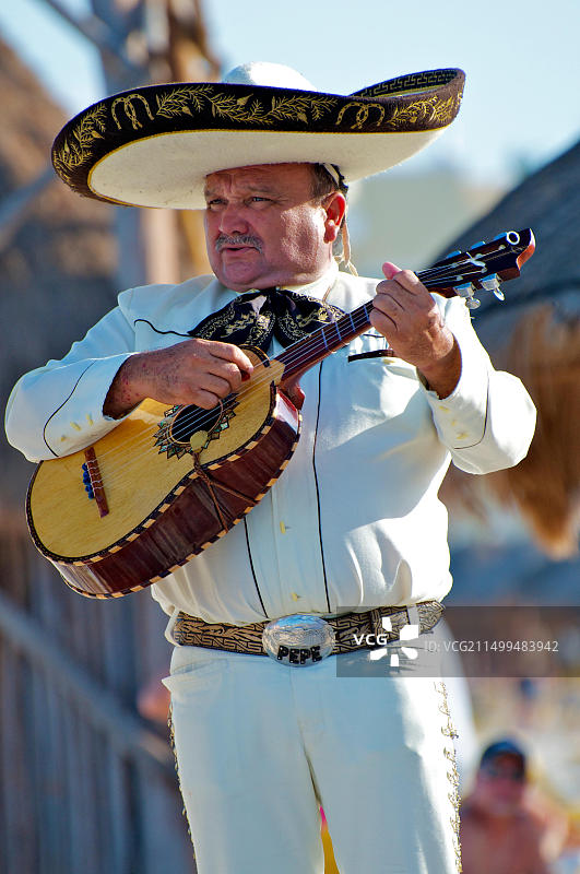 在墨西哥阳光明媚的海滩上，头戴阔边帽、身穿金色套装的墨西哥流浪乐队吉他手在婚礼上表演图片素材