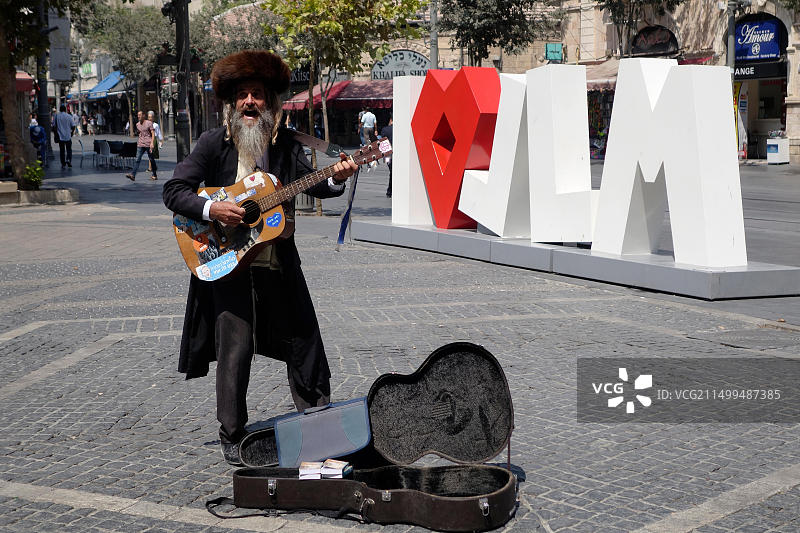 在耶路撒冷雅法路锡安广场，一位正统犹太教街头艺人在公共雕塑“爱”前弹吉他歌唱图片素材
