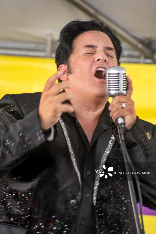 在加利福尼亚州富勒顿音乐节上，装扮成猫王模仿者的男人手持麦克风演唱摇滚歌曲图片素材