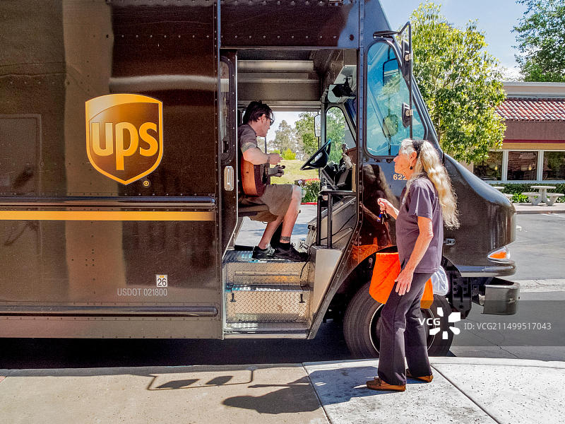 美国联合包裹运送服务公司（UPS）司机在加利福尼亚州拉古纳尼格尔的购物中心送货间隙弹吉他，一位路人欣赏他的音乐图片素材