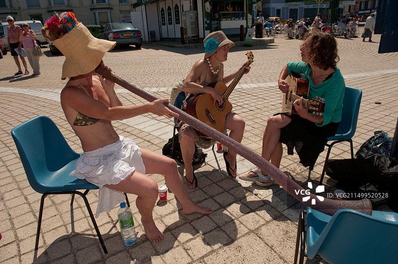 一位年轻女子在英国威尔士阿伯里斯特威斯海滨长廊上演奏迪吉里杜管和两把原声吉他图片素材