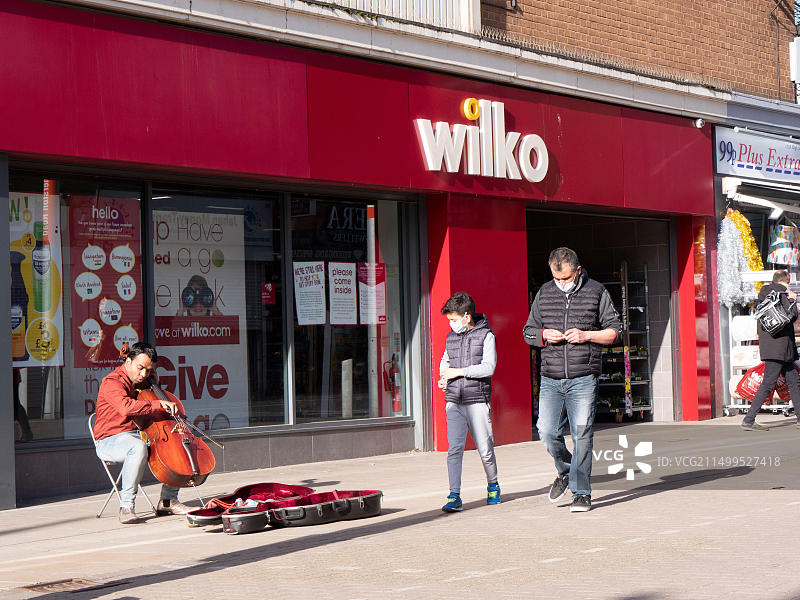 伦敦沃尔瑟姆森林沃尔瑟姆stow高街的Wilko商店，有购物者和街头艺人演奏大提琴图片素材