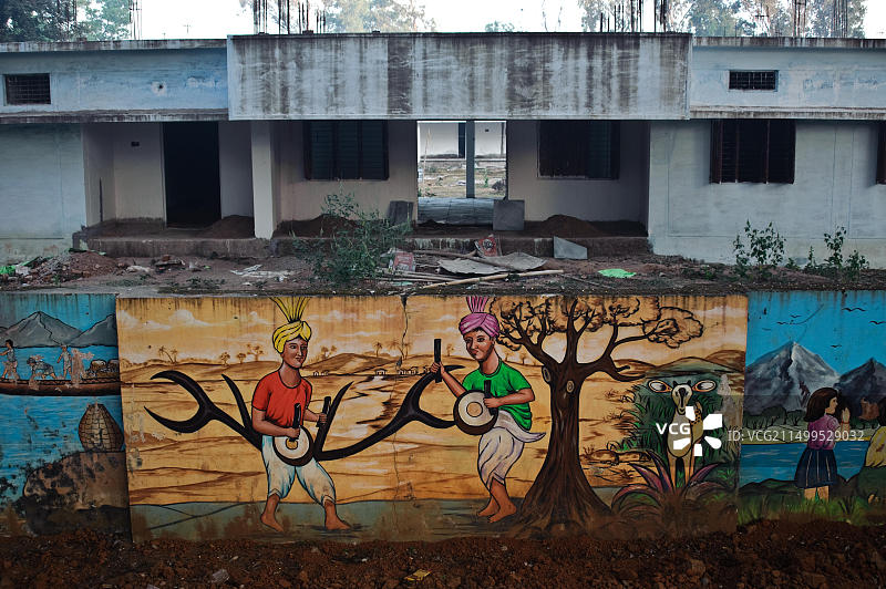 描绘自然中击鼓部落男子的壁画，背景是维修中的学校图片素材