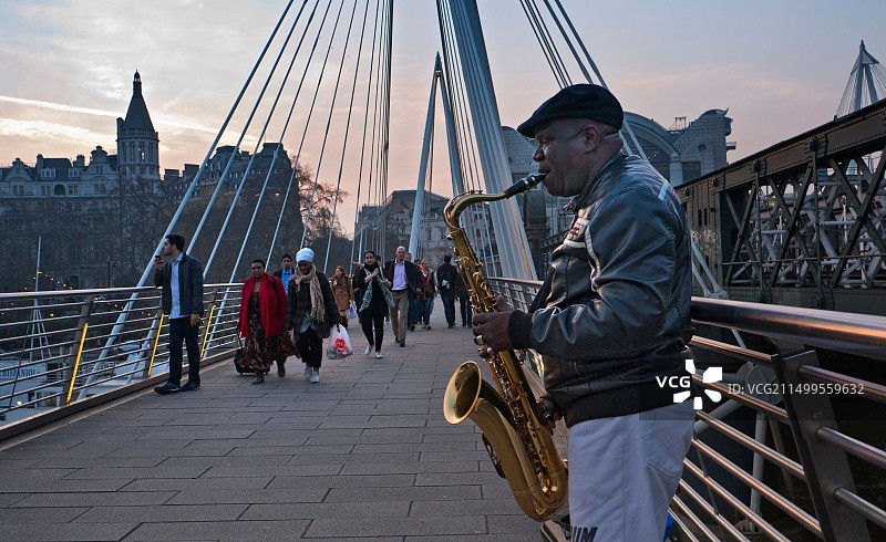 伦敦英国金色禧年桥上在日落时演奏萨克斯管的街头艺人图片素材