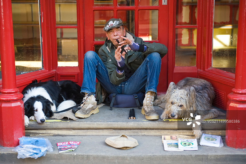 在英国什罗普郡勒德洛食品节期间，男人坐在门口和两条狗一起吹长笛图片素材