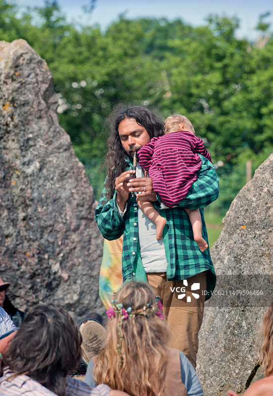 2013年英国格拉斯顿伯里音乐节：男子与孩子在立石旁吹奏管乐图片素材