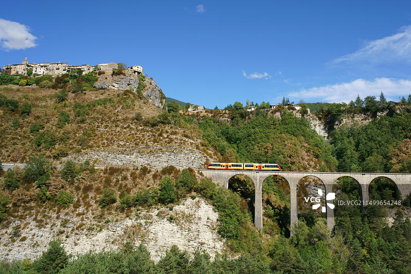 法国上普罗旺斯阿尔卑斯省梅阿耶：石拱高架桥上的通勤列车与中世纪村庄图片素材