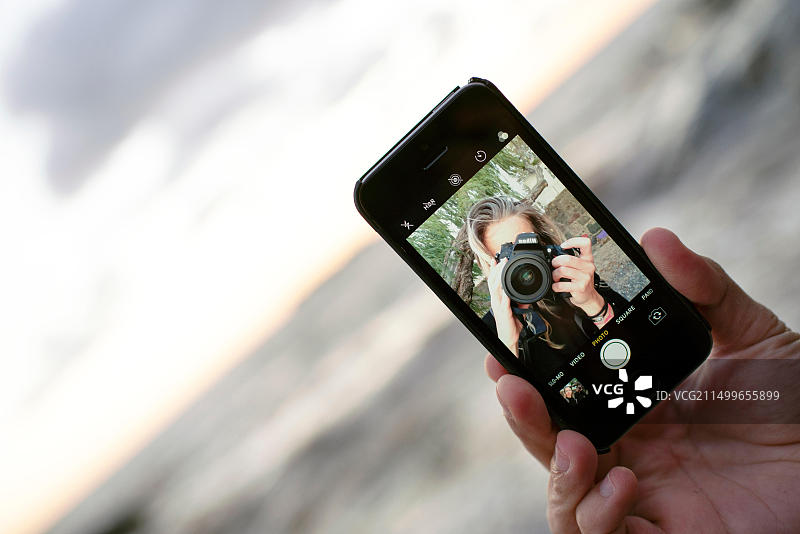 女摄影师自拍，男子手持智能手机。智能手机摄影，旅行/户外生活方式图片素材