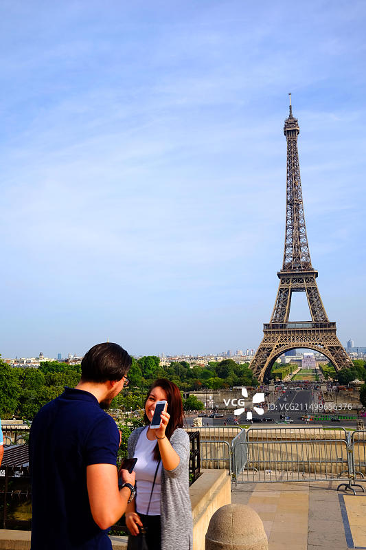 年轻情侣在巴黎埃菲尔铁塔前用智能手机自拍图片素材