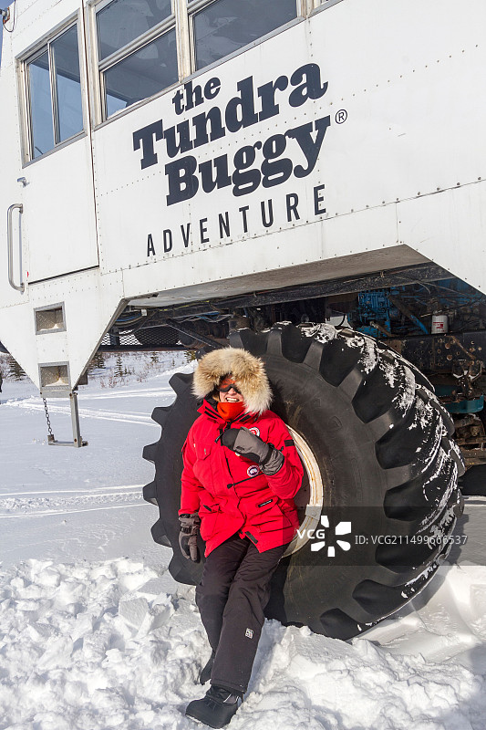 游客站在苔原越野车使用的巨大轮胎旁，这种车用于在丘吉尔附近的苔原上观光图片素材