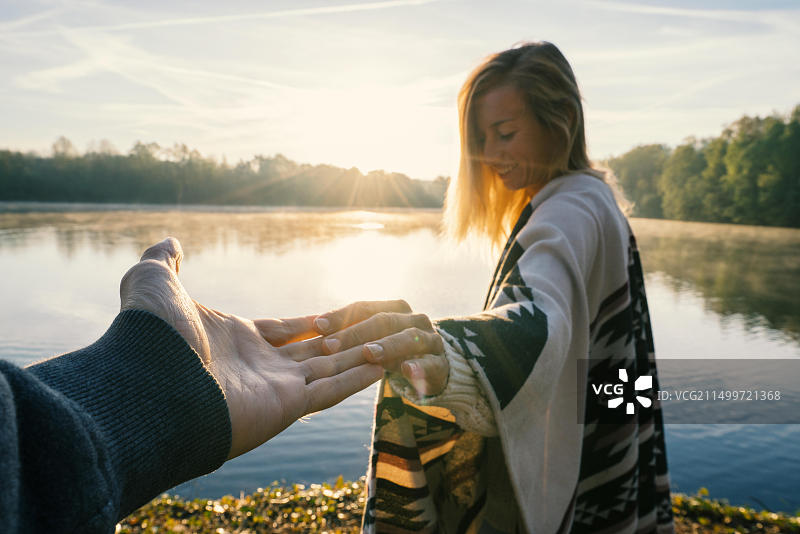 年轻女子在日出时牵着男友的手走向湖边图片素材