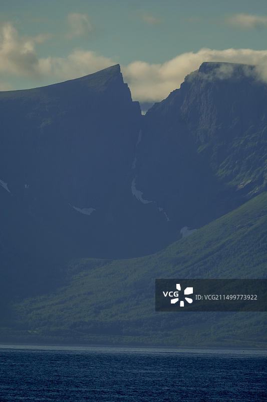 阳光下海面上的岩石山峰，位于挪威图片素材