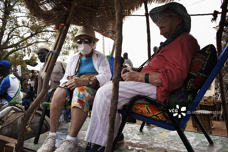 年长的旅行者在西非马里乘坐驴车旅行，其中一人戴着口罩。图片素材