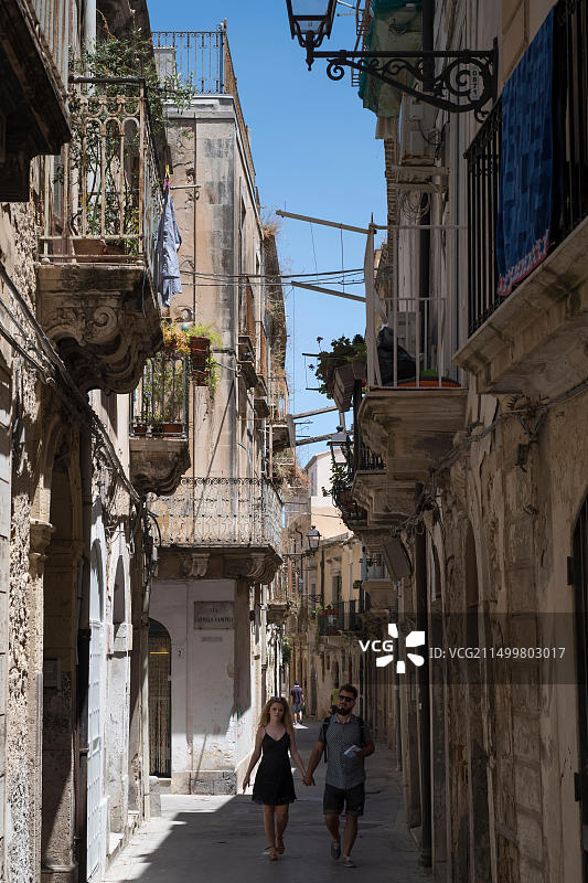 西西里锡拉库萨奥尔蒂贾区迪奥内大街，年轻夫妇在华丽小巷中漫步的街景图片素材