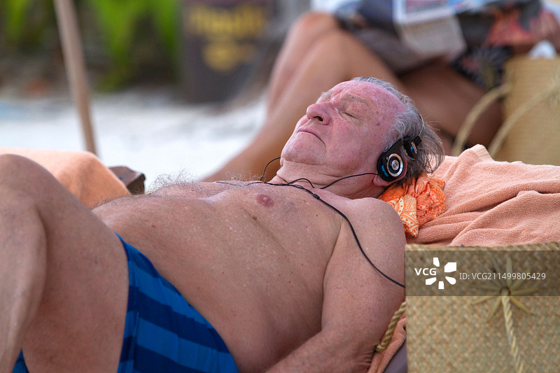年长的男人戴着耳机在泰国苏梅岛查汶海滩享受日光浴图片素材
