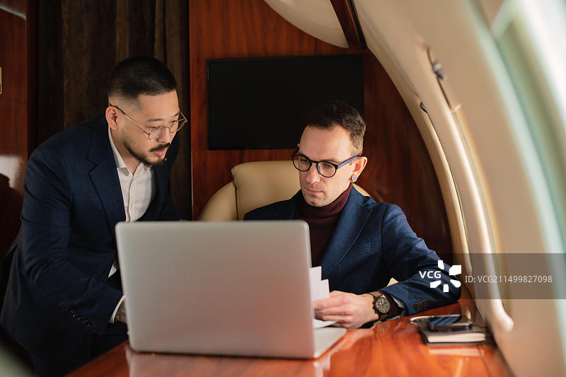 优雅的商务人士夫妇在私人飞机上谈论工作，观看笔记本电脑图片素材