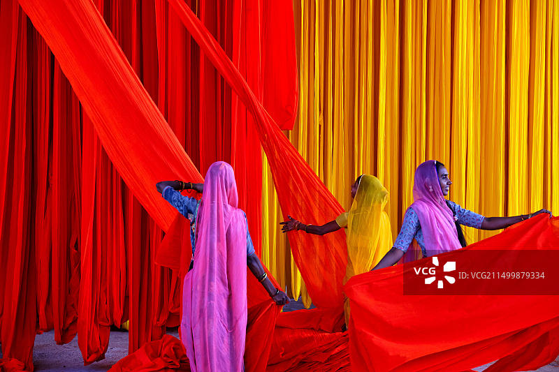 印度拉贾斯坦邦纱丽工厂：露天晾晒纺织品，妇女们叠放干燥的纺织品图片素材