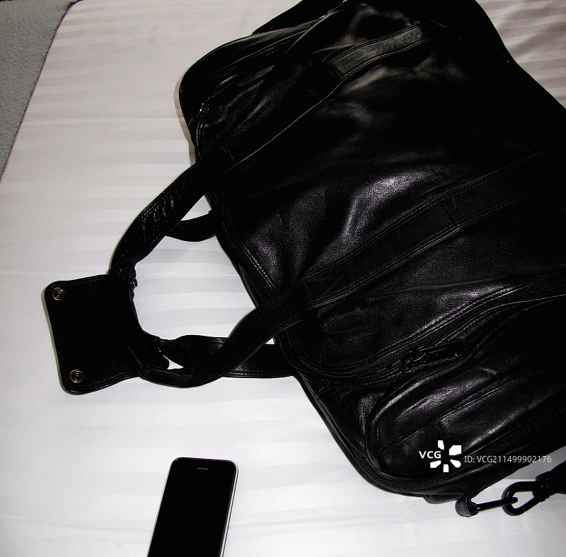 皮革旅行包和酒店床上的iPhone图片素材