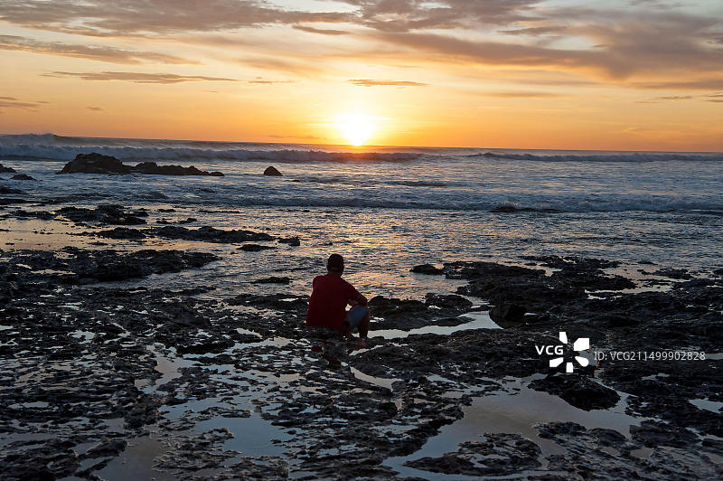 男子在哥斯达黎加海滩的岩石潮汐池中欣赏绚丽的日落图片素材