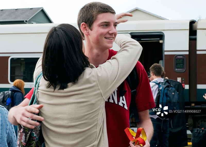年轻男人乘火车旅行抵达，一位年轻女人拥抱迎接图片素材