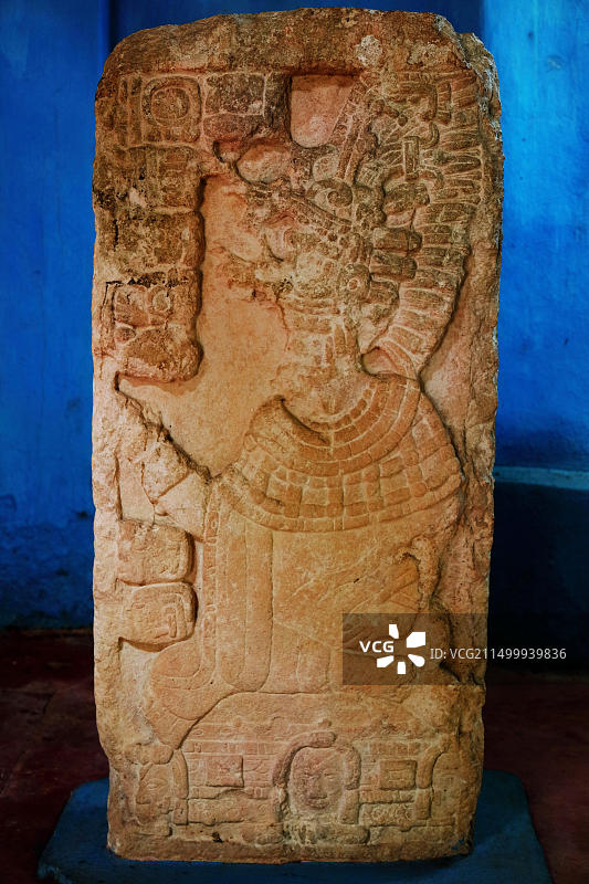 石碑20描绘了一位罕见的坐姿领导者，他戴着精致的面具和头饰，而象形文字则沿着石头左侧的古代M延伸图片素材