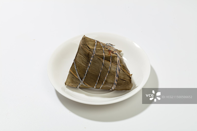 白色背景上，盘子里摆放着一个捆扎好了的粽子图片素材