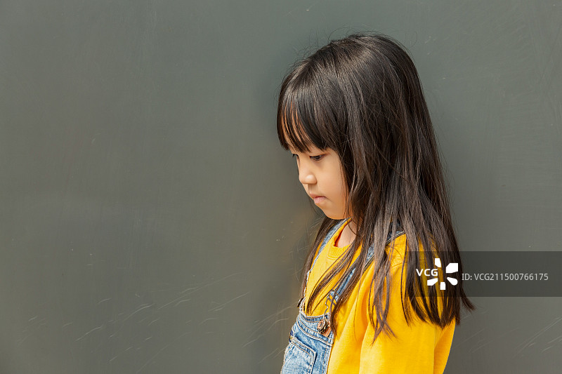 站在灰色背景墙前的不开心的中国小女孩图片素材