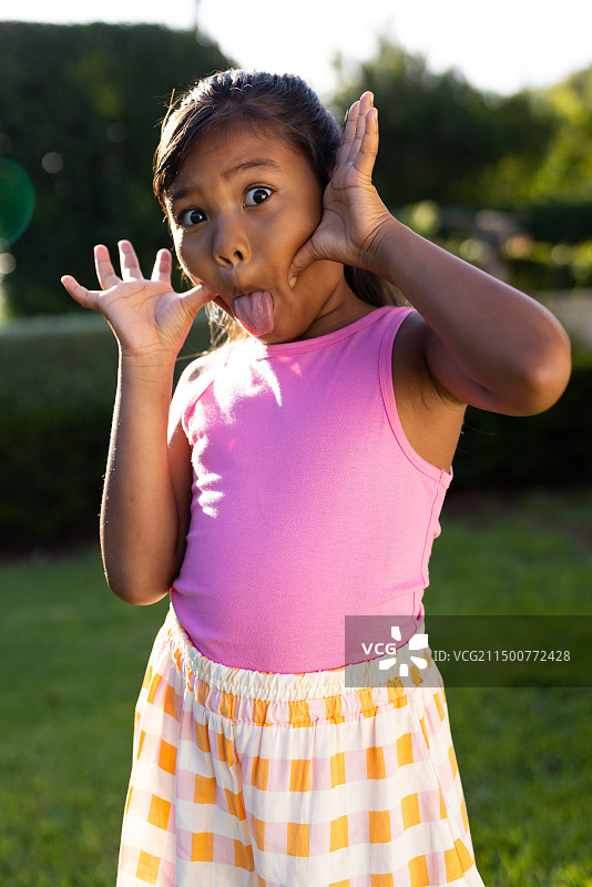 户外，年轻的混血女孩双手放在脸颊上做鬼脸图片素材