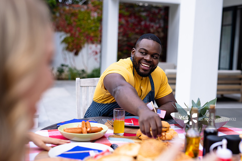 幸福的多元朋友在阳台上聊天和共进晚餐，有美国国旗图片素材