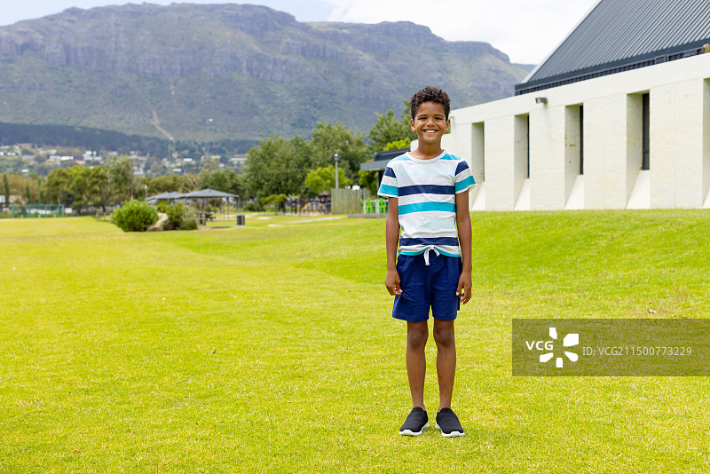 在阳光明媚的草地上微笑的混血男孩，背景是山，有文案空间图片素材